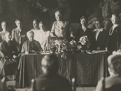 A-F-NLK16-00045 Generalversammlung des Deutschen Evangelischen Frauenbundes in Stralsund vom 08.-13.04.1927. In der ersten Reihe sind Selma von der Groeben (2. v. links), Paula Mueller-Otfried (am Pult stehend), Adelheid von Bennigsen und Auguste Jorns zu sehen, gemeinfrei.